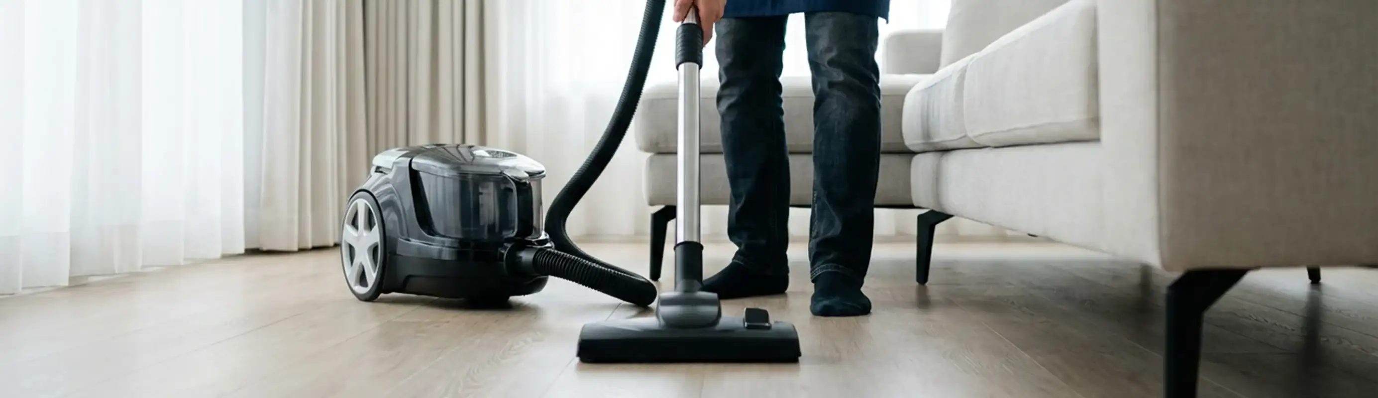 Professional house cleaner vacuuming a living room floor with a canister vacuum cleaner, Pembroke Pines, FL.