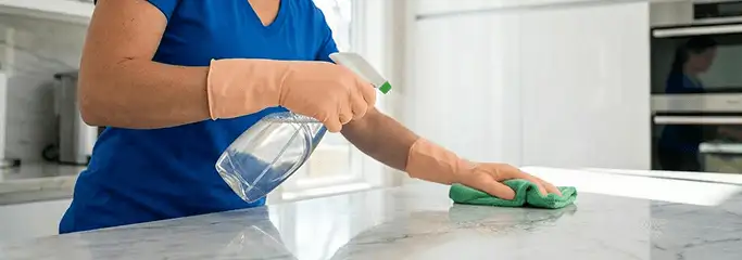 Maid service worker spraying and wiping a kitchen countertop with a microfiber cloth for sanitizing, Pembroke Pines, FL.