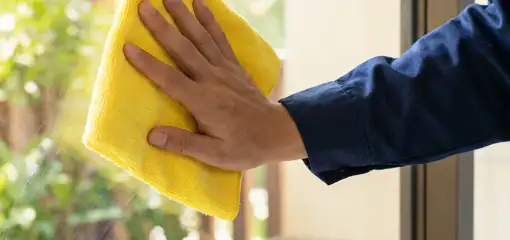 House cleaner wiping a glass window with a yellow microfiber cloth for streak-free cleaning, Pembroke Pines, FL.